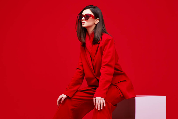 Fashion model in red suit and sunglasses. Studio shot. - 写真・画像