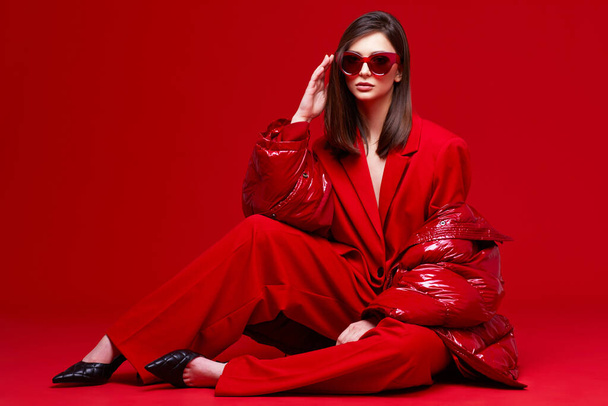 Fashion model in red suit, down jacket and sunglasses. Studio shot. - Fotografie, Obrázek