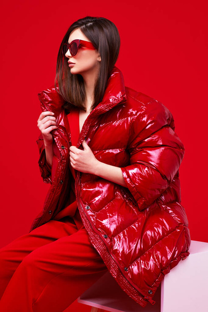Fashion model in red suit, down jacket and sunglasses. Studio shot. - Foto, immagini