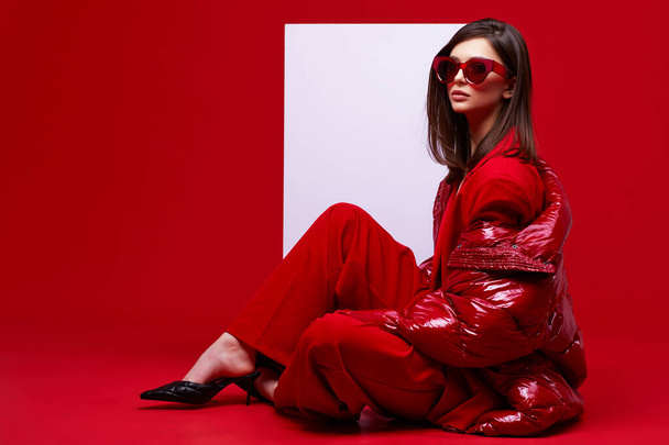 Fashion model in red suit, down jacket and sunglasses. Studio shot. - Photo, Image