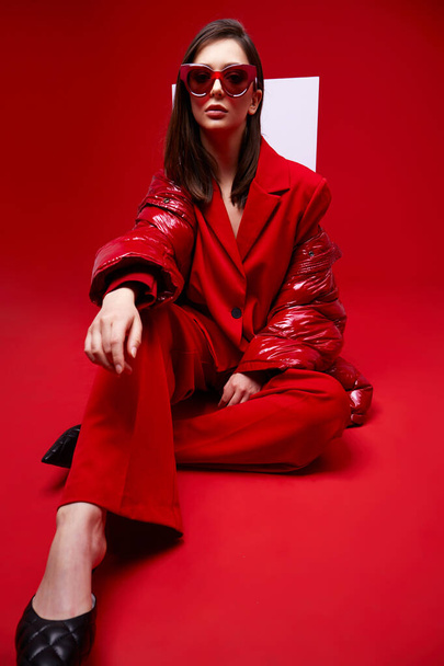 Fashion model in red suit, down jacket and sunglasses. Studio shot. - Fotó, kép