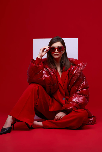 Fashion model in red suit, down jacket and sunglasses. Studio shot. - Фото, зображення