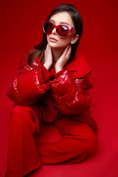 Fashion model in red suit, down jacket and sunglasses. Studio shot. - Foto, imagen