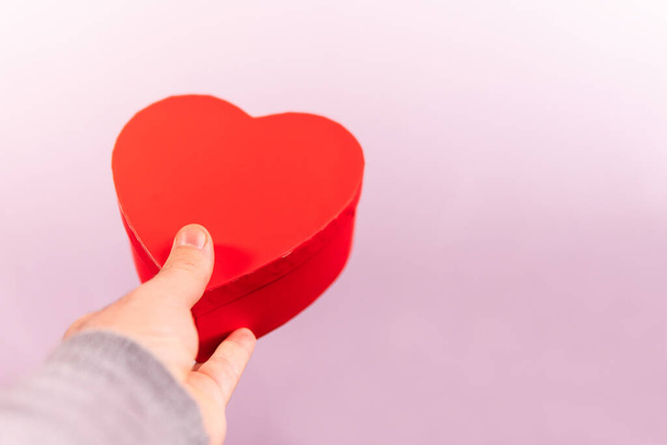 A hand holding a heart shaped gift box on a pink background - copy space - Φωτογραφία, εικόνα