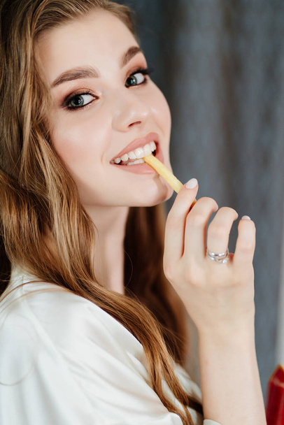 beautiful young woman with long hair and makeup eating French fries. - Fotoğraf, Görsel