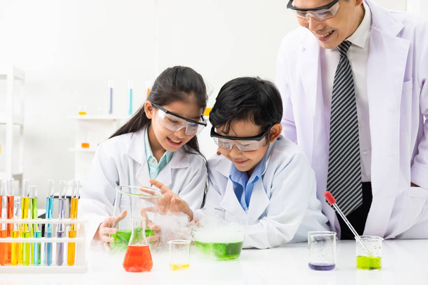 Junge asiatische Jungen und Mädchen tragen Schutzgoogle, während sie im Klassenzimmer mit dem Lehrer naturwissenschaftliche Experimente durchführen. Lernen und Spaß haben. Konzept Chemiker oder Biologie.  - Foto, Bild