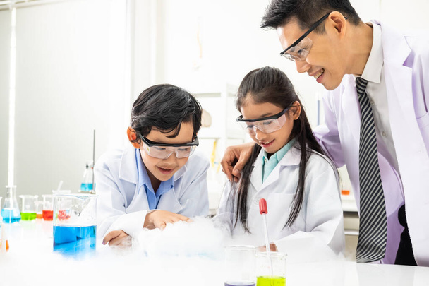 Young Asian boy and girl student wearing protective google while study and do science experiment in classroom with teacher. Learning and having fun moment. Chemist or biology classroom concept.  - Фото, зображення
