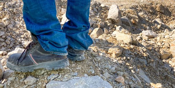 産業鉱山内の岩の上に立って重労働産業用ブーツを身に着けている男性の水平バナーショット。保護と安全のためのハード作業条件のための耐久性のある作業服 - 写真・画像