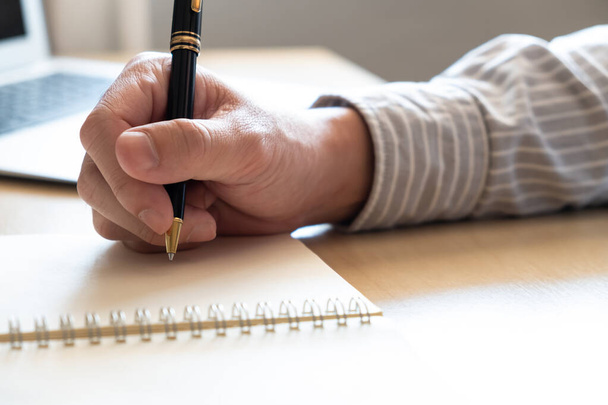 ペンを使用して人間の手で選択的なフォーカスは、作業台の上に紙に短いメモを書きます。背景にぼやけたラップトップコンピュータで。営業日中の計画または編成活動の一覧. - 写真・画像