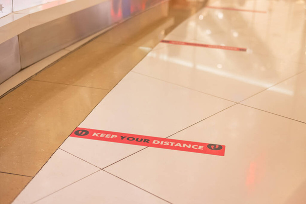 Szelektív fókusz piros jel a padlón a nyilvános területen, amely elősegíti és bátorítja az embereket, hogy tartsák a távolságot egymástól, hogy megakadályozzák Covid vagy Coronavirus. Új, normális, társadalmi távolságtartó koncepció. - Fotó, kép