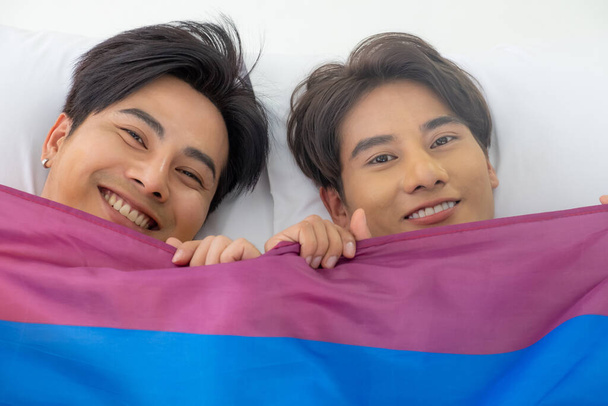 Selective focus at face. Handsome young Asian gay homosexual couple. Hug and embrace on the bed. With rainbow flag as LGBT sign. Gender equality and right. Romantic moment, same sex relationship. - Photo, Image