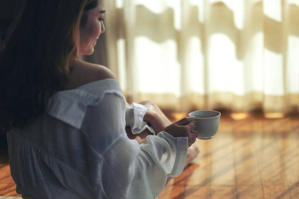 een vrouw die op de vloer zit en 's morgens een kop hete koffie drinkt - Foto, afbeelding