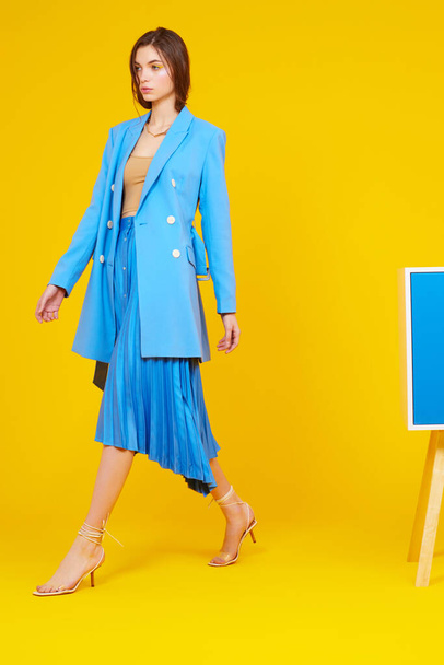 High fashion portrait of young elegant woman in blue jacket and skirt. Yellow background, studio shot - Zdjęcie, obraz