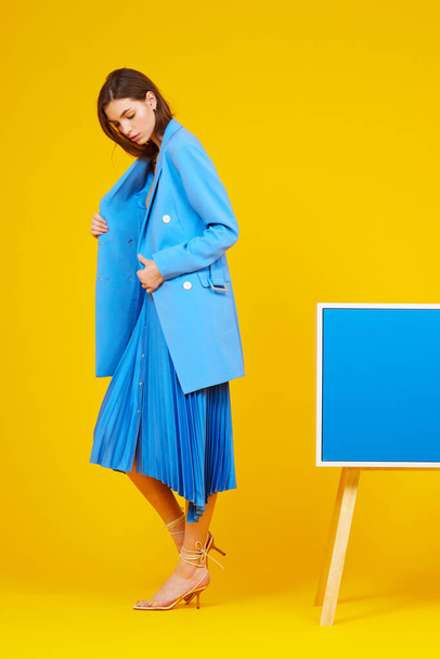 High fashion portrait of young elegant woman in blue jacket and skirt. Yellow background, studio shot - Foto, imagen