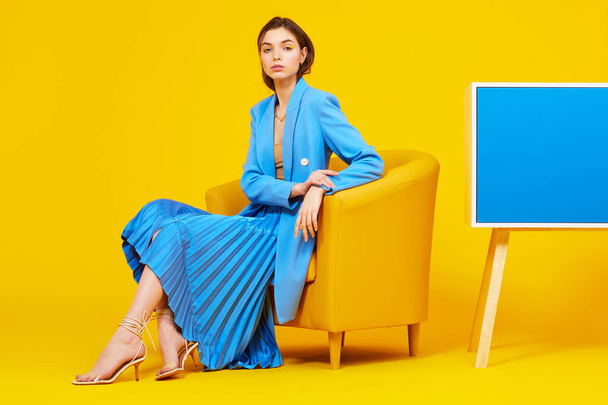 High fashion portrait of young elegant woman in blue jacket and skirt. Yellow background, studio shot - Фото, изображение