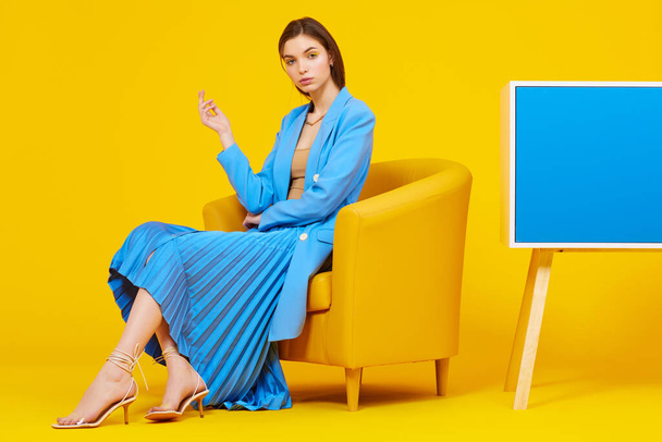 High fashion portrait of young elegant woman in blue jacket and skirt. Yellow background, studio shot - Foto, Imagen