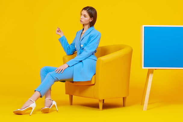 High fashion portrait of young elegant woman in blue suit. Yellow background, studio shot - 写真・画像