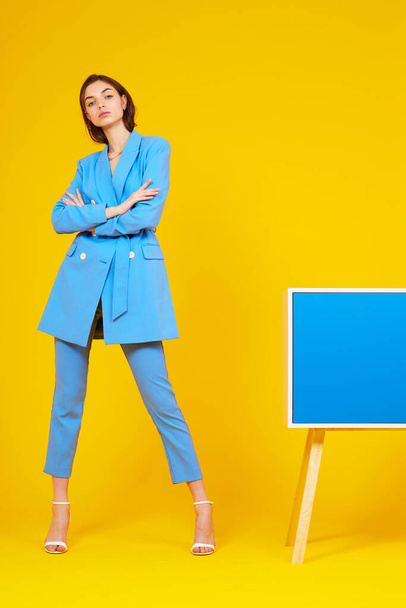 High fashion portrait of young elegant woman in blue suit. Yellow background, studio shot - Fotó, kép
