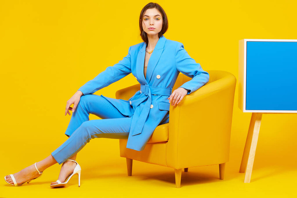 High fashion portrait of young elegant woman in blue suit. Yellow background, studio shot - Foto, imagen