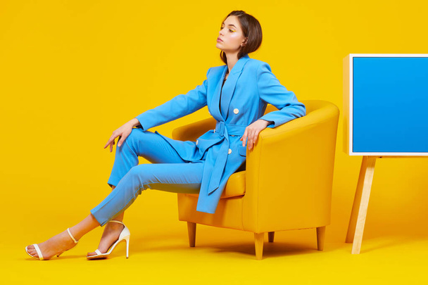 High fashion portrait of young elegant woman in blue suit. Yellow background, studio shot - Fotó, kép