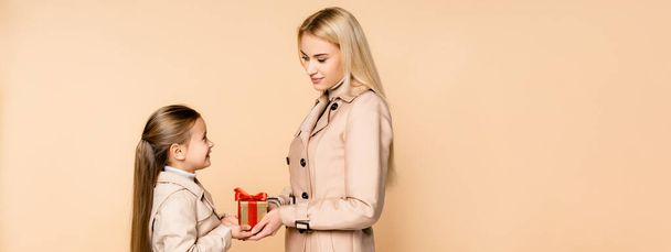 cheerful kid giving present to happy mother on 8 march isolated on beige, banner - Фото, изображение