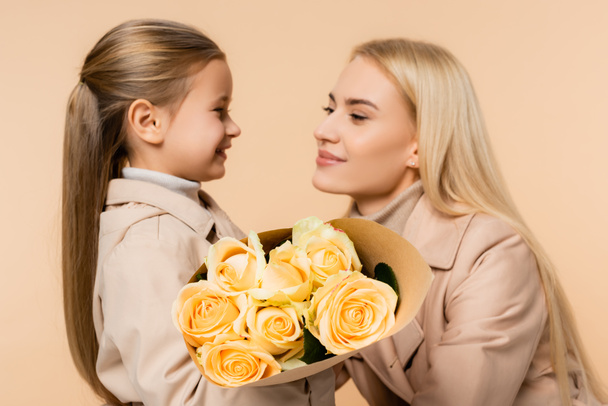 yellow roses in hands of child near mother on 8 march and blurred background isolated on beige - Photo, Image