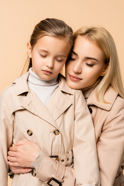 zorgzame moeder en dochter met gesloten ogen knuffelen geïsoleerd op beige - Foto, afbeelding