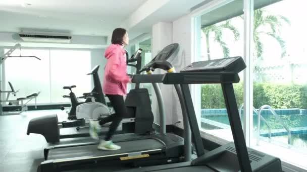 Fitness Asiatin im rosafarbenen Mantel läuft auf Laufband, Marathontraining im Fitnessstudio - Filmmaterial, Video