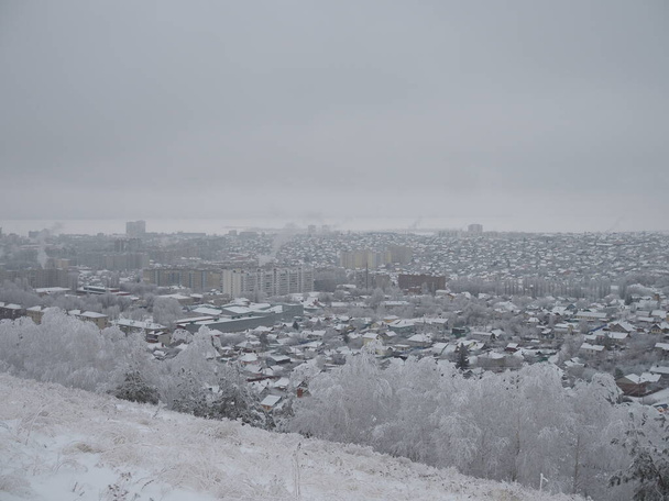 曇り空の冬の日の地平線の雪に覆われた都市や都市の家の眺め. - 写真・画像