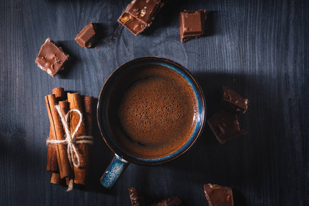 Krásný keramický modrý šálek s horkou kávou a kousky čokolády na dřevěném černém stole - Fotografie, Obrázek