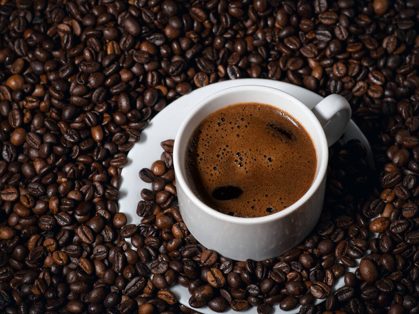 Detailní záběr bílého espresso šálku na stole se spoustou kávových zrn - Fotografie, Obrázek