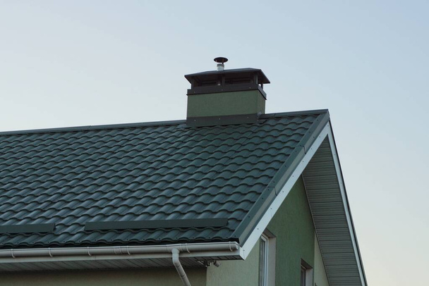 parte del techo de una casa privada bajo azulejos verdes con una chimenea de hormigón contra un cielo gris - Foto, Imagen
