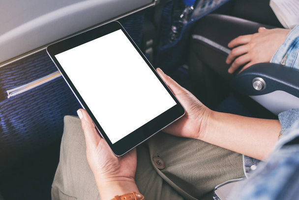 Mockup image of a woman holding and looking at black tablet pc with blank white desktop screen while sitting in the cabin - Photo, image