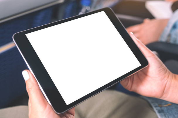 Immagine ridicola di una donna che tiene in mano e guarda il tablet PC nero con schermo bianco vuoto mentre è seduta in cabina - Foto, immagini