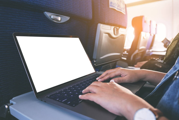 Immagine mockup di una donna che usa e digita sul computer portatile con schermo bianco vuoto mentre è seduta in cabina - Foto, immagini