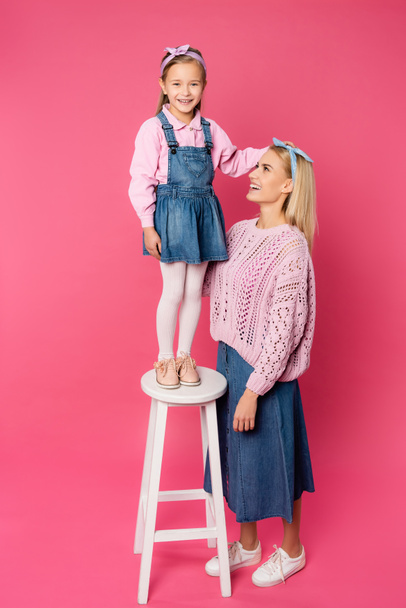 happy kid standing on chair near smiling mother on pink - 写真・画像