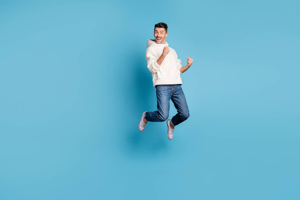 Full size photo of young happy excited crazy positive man jumping hold fists in victory isolated on blue color background - 写真・画像