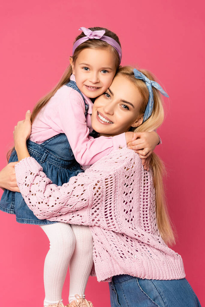 glückliche Tochter lächelt, während umarmt Mutter isoliert auf rosa - Foto, Bild