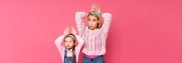 mother and daughter making bunny ears with hands isolated on pink, banner - Foto, Imagem