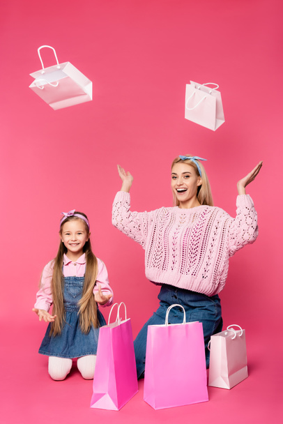 asombrados madre e hija sonriendo cerca de bolsas de compras en rosa - Foto, Imagen