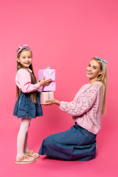 happy mother smiling near daughter holding presents on pink - Foto, immagini