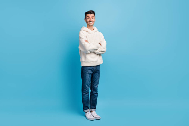 Photo portrait full body view of turned man with crossed arms wearing woolen hoodie isolated on pastel blue colored background - 写真・画像