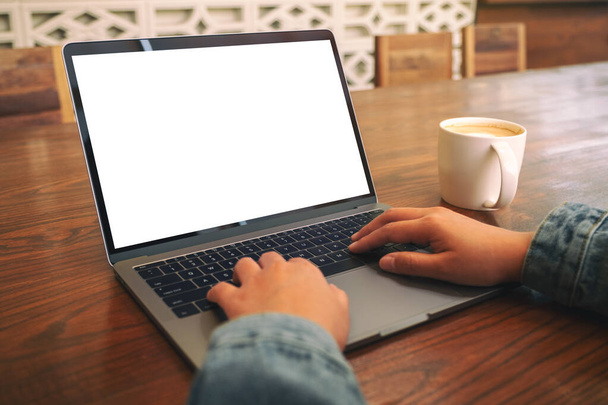 Mockup-Bild einer Frau, die Laptop mit leerem weißen Bildschirm und Kaffeetasse auf Holztisch benutzt und tippt - Foto, Bild