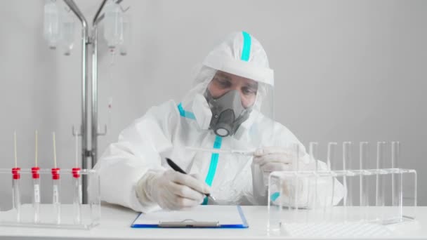 Trabajador médico en PPE que trabaja con la prueba COVID-19 en el laboratorio del hospital, anotando los resultados. - Imágenes, Vídeo