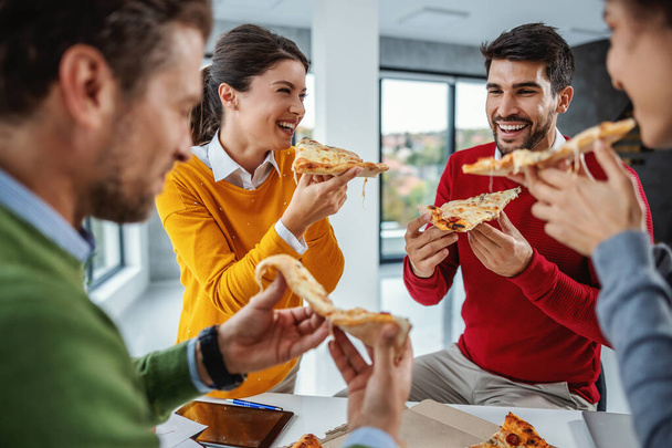 Aufgeregte multikulturelle Gruppe von Geschäftsleuten, die im Sitzungssaal stehen und mittags Pizza essen. - Foto, Bild