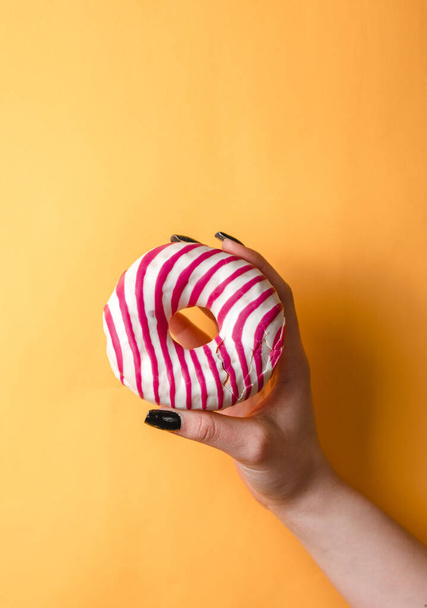gele achtergrond, donut in de hand, meisje - Foto, afbeelding