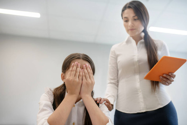 Girl hiding face and teacher with tablet - Фото, зображення