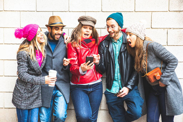 友人のグループは、彼らの携帯電話で遊ぶ。友人グループはソーシャルメディアで楽しみを共有しています。技術で遊ぶミレニアル世代。テクノロジーの概念への依存。スマートフォンを見ている若い友達. - 写真・画像