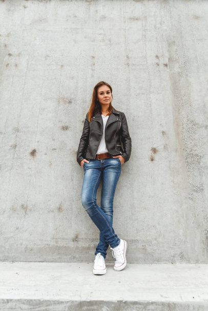 Retrato de uma menina bonita em jeans e uma jaqueta de couro preto da parede de concreto - Foto, Imagem