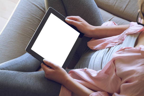 Woman sitting on sofa uses tablet, holding in hands - Foto, immagini